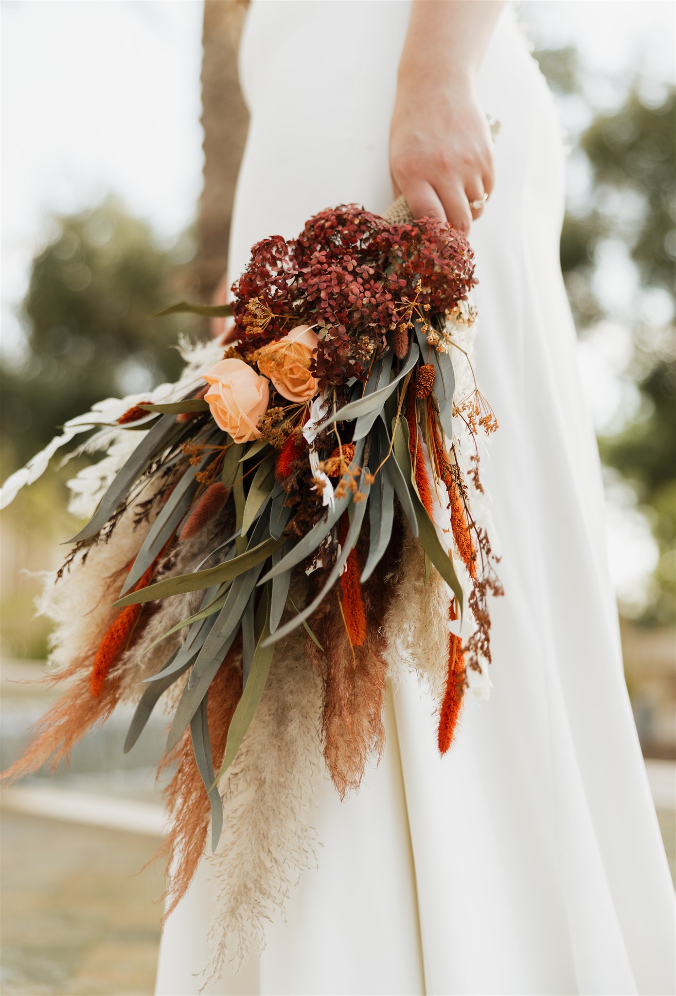 Details of a bride's boho style bouquet as she holds it at her side at sunset