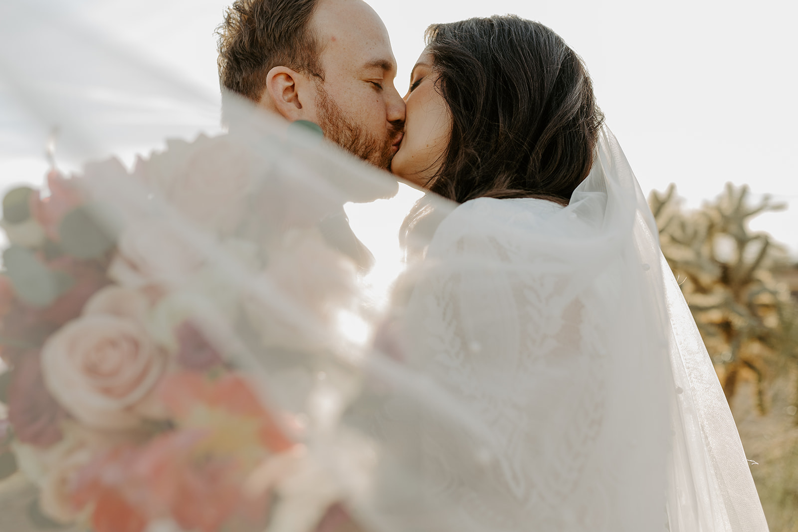 Newlyweds kiss in the desert at sunset as the veil flows around them at El Chorro wedding venue