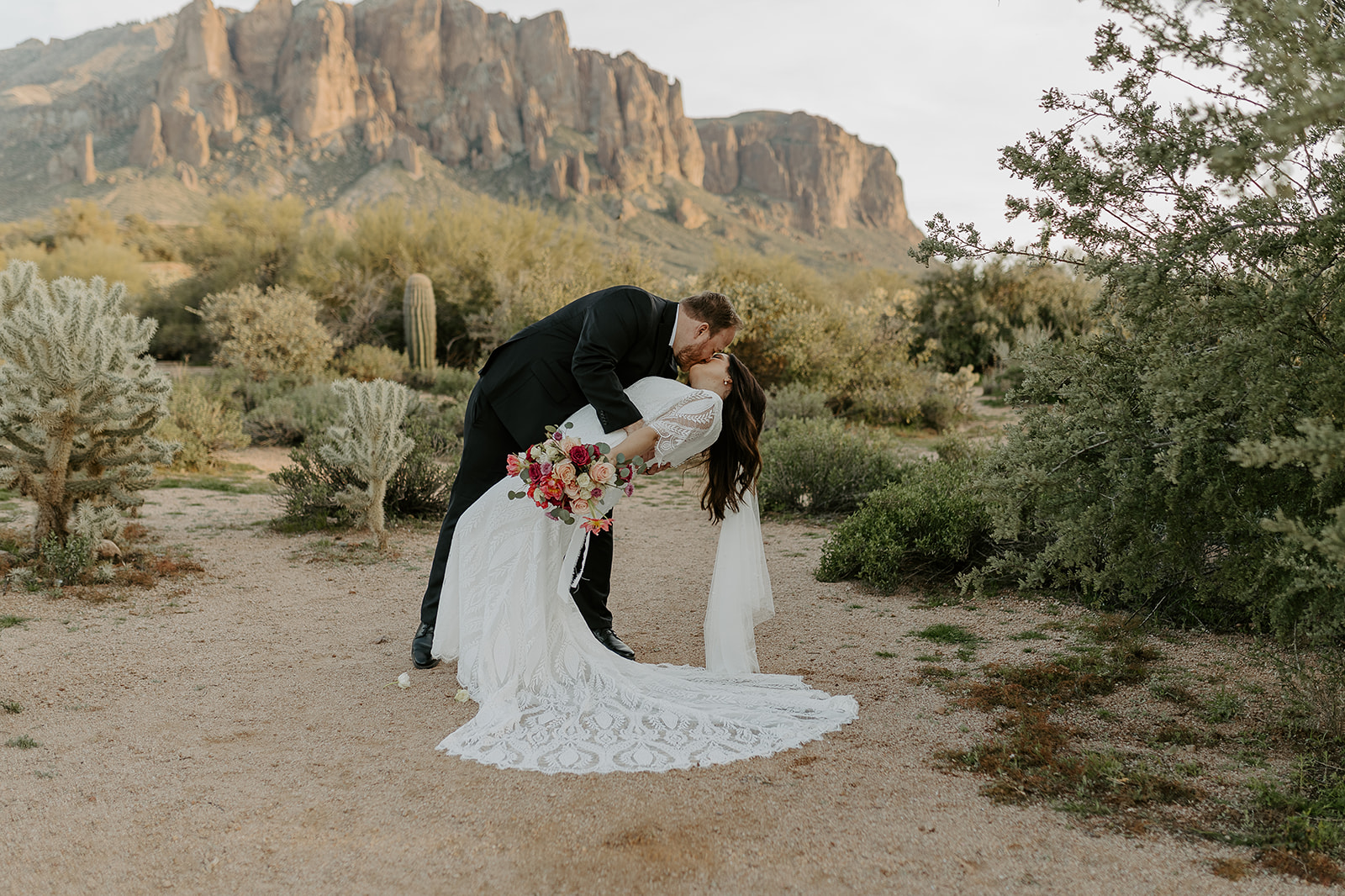 A groom in black dips his bride for a kiss in the desert at sunset during their El Chorro wedding