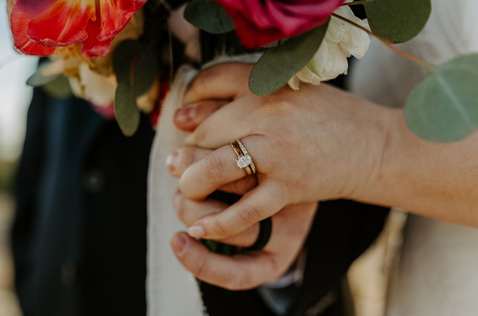 Details of a bride's rings on her finger while holding a bright bouquet