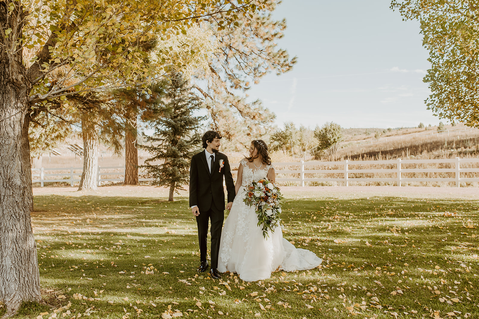 Newlyweds walk holding hands and smiling at each other in a lawn in fall at legacy lodge in Heber, AZ
