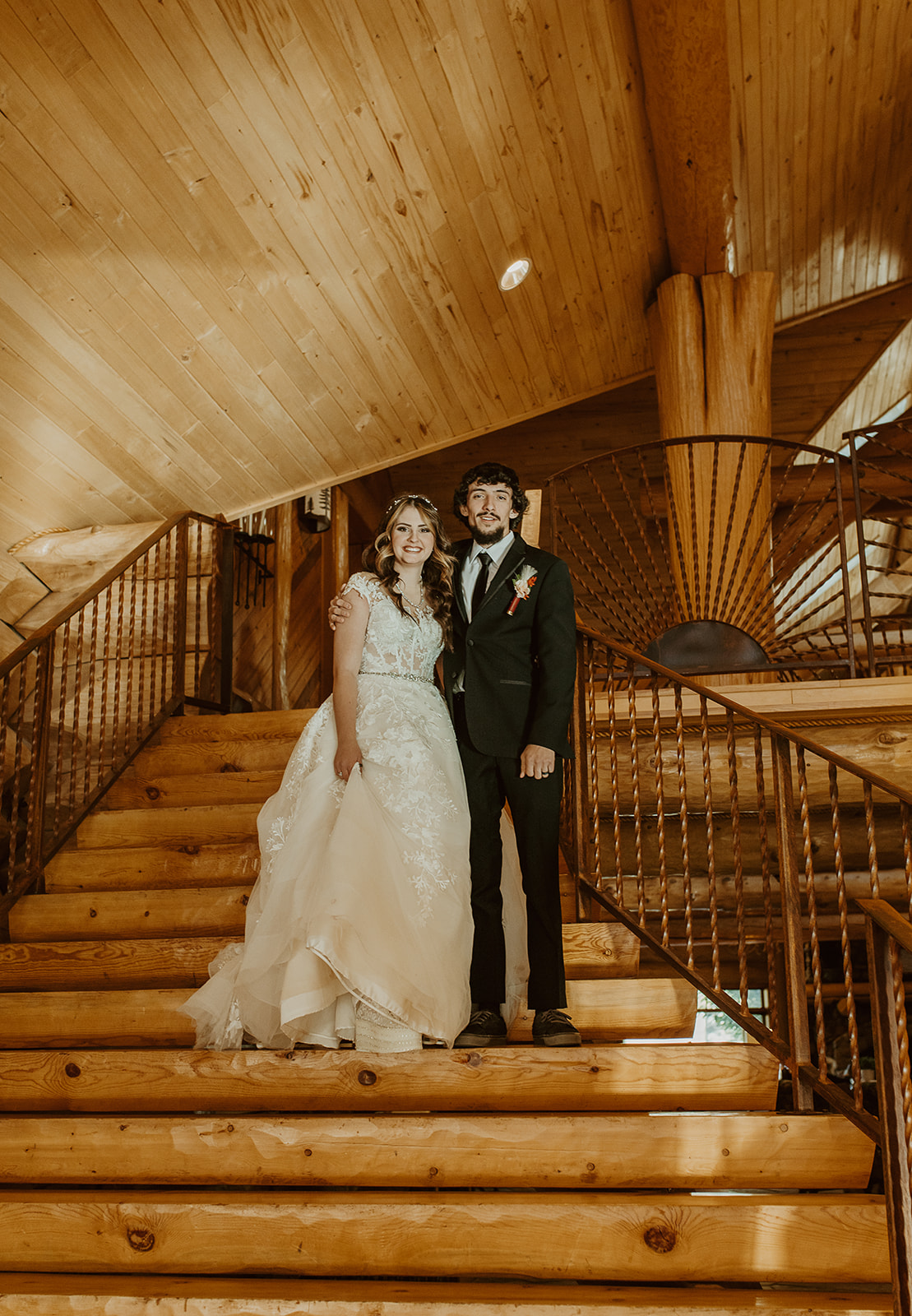 Newlyweds smile on the grand wooden staircase with arms around each other at legacy lodge in Heber, AZ