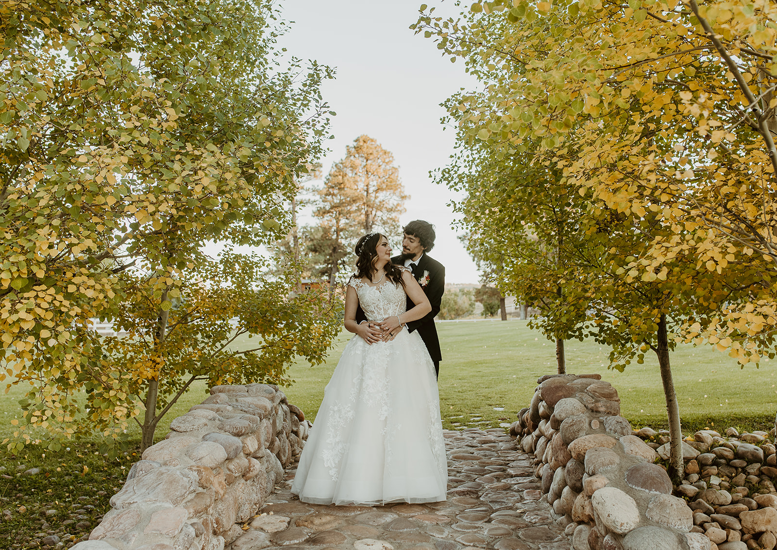 Happy newlyweds snuggle on a stone bridge framed in yellow trees at legacy lodge in Heber, AZ