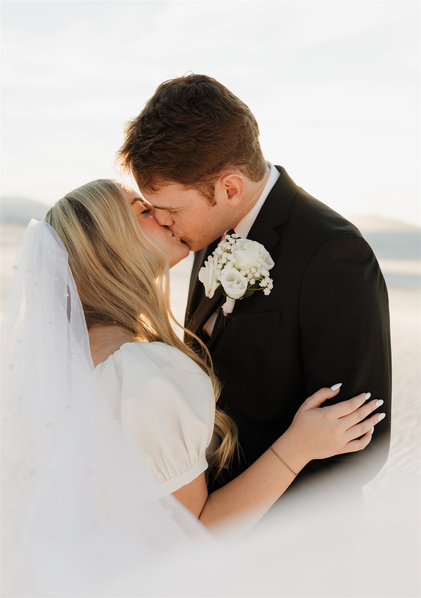 Newlyweds happily kiss at sunset as the veil flows around them at The Ashley Castle wedding venue