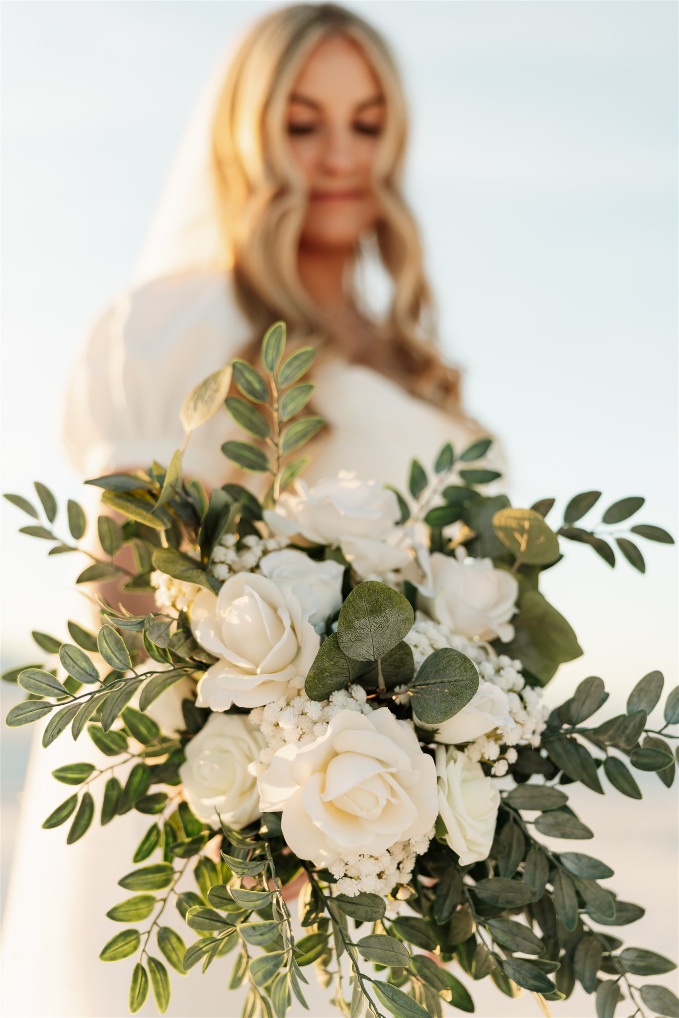 Details of a bride's white rose bouquet as she holds it out in front of her at sunset