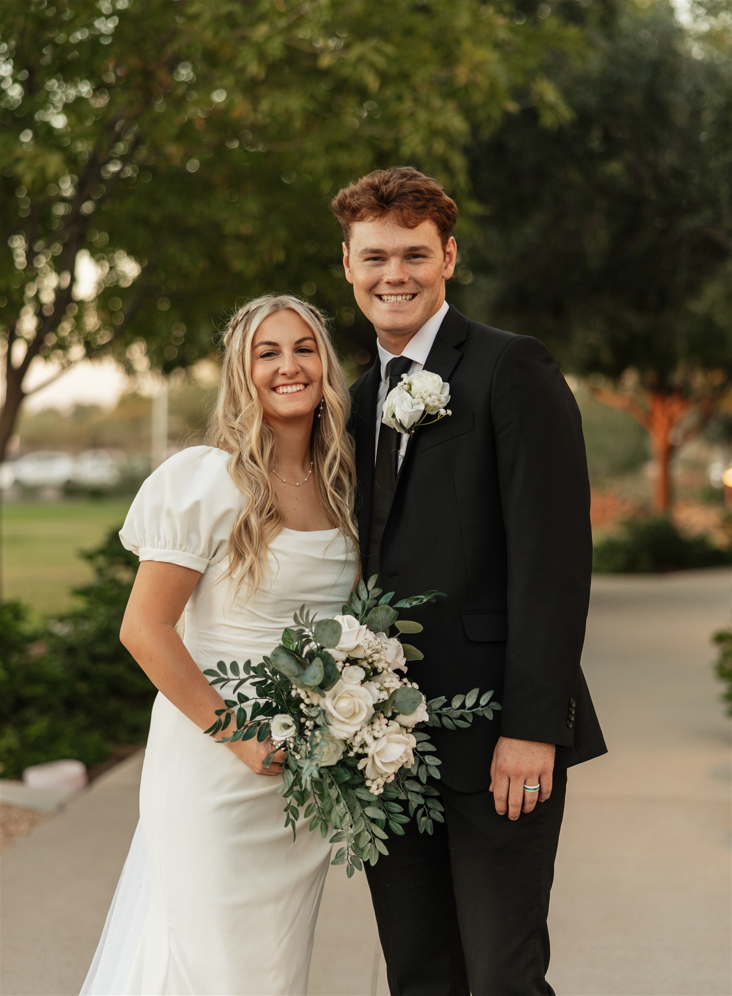 Happy newlyweds stand in a park sidewalk smiling during their celebration at The Ashley Castle wedding venue