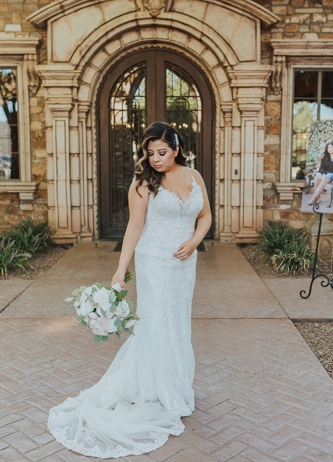A bride stands gazing down to her white bouquet in the grand entrance to her Villa Siena wedding
