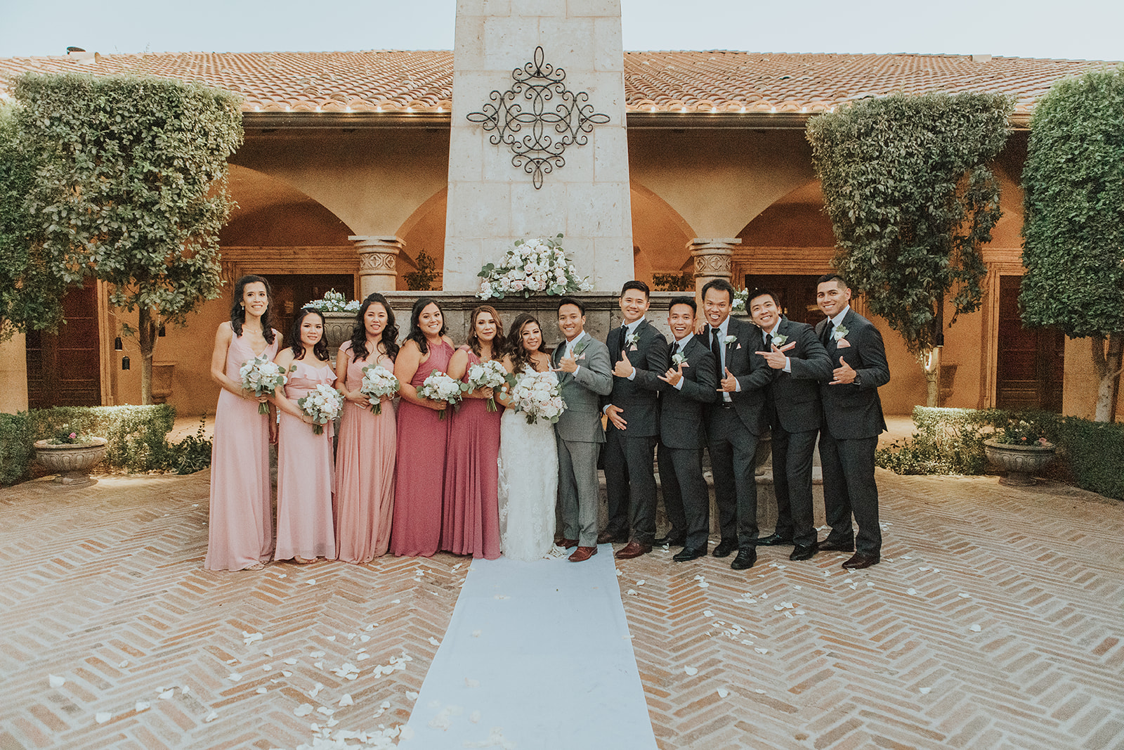 A bride and groom stand with their bridesmaids in pink and groomsmen in black in a patio
